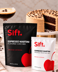 Two Sift. Espresso Martini flavored cake mix pouches, one black and one white, displayed on a marble surface with coffee beans, a cocktail glass, and a layered chocolate cake in the background.