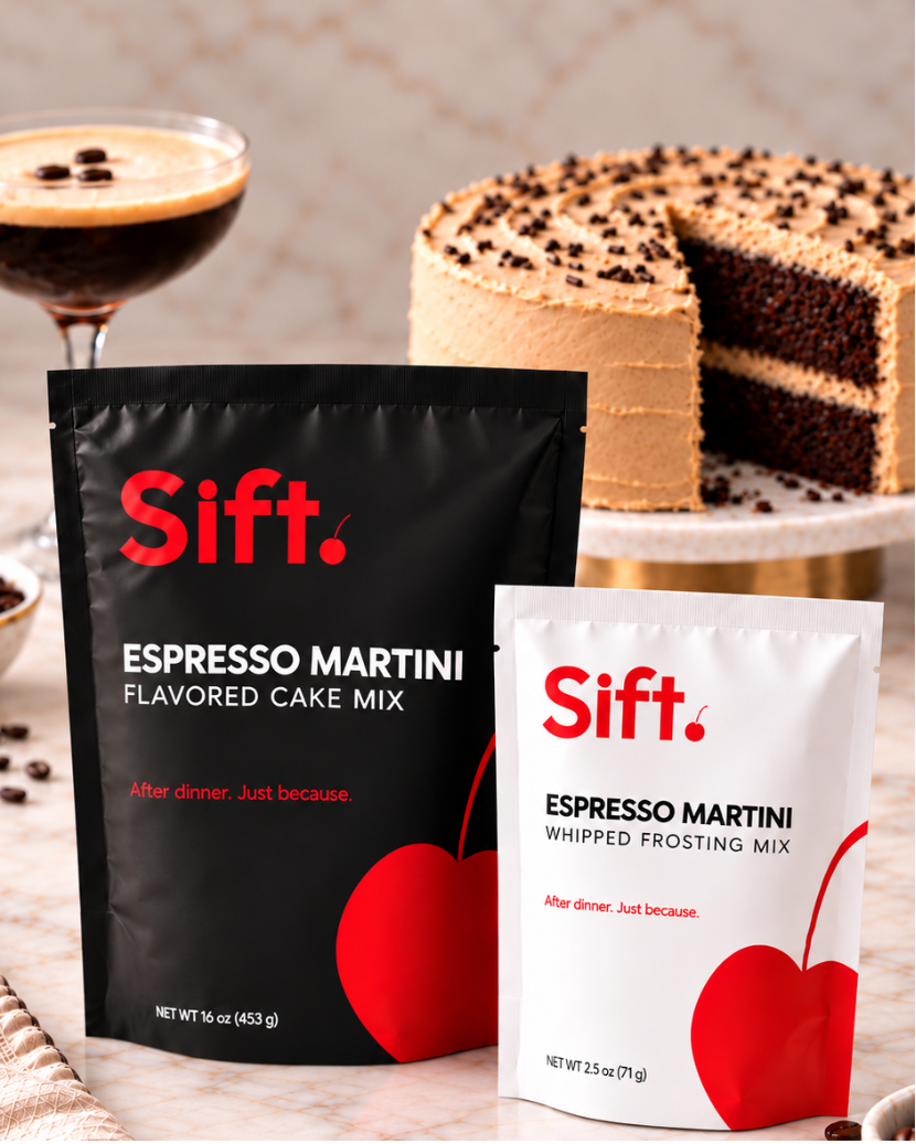 Two Sift. Espresso Martini flavored cake mix pouches, one black and one white, displayed on a marble surface with coffee beans, a cocktail glass, and a layered chocolate cake in the background.